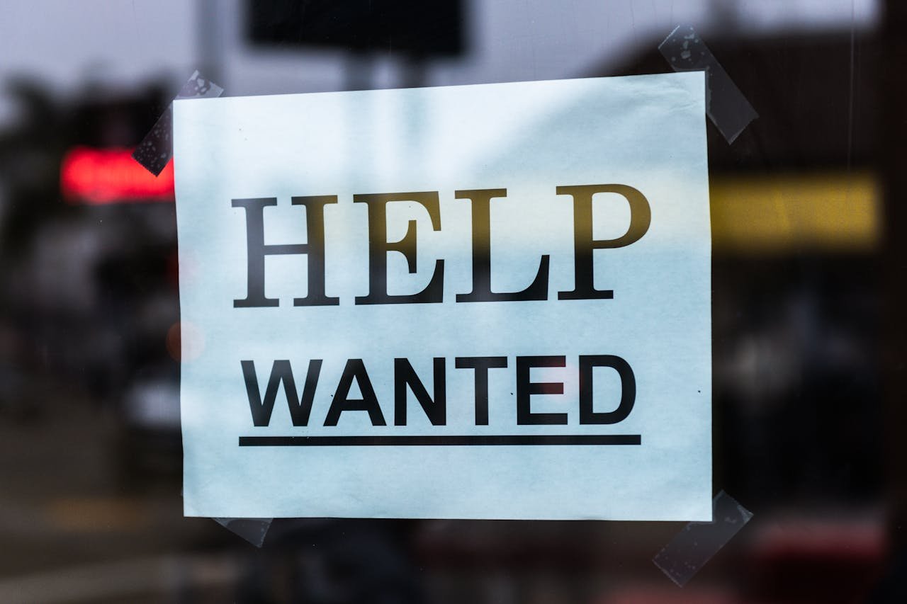 about-02 Close-up of a Help Wanted sign taped to a glass window in a storefront.